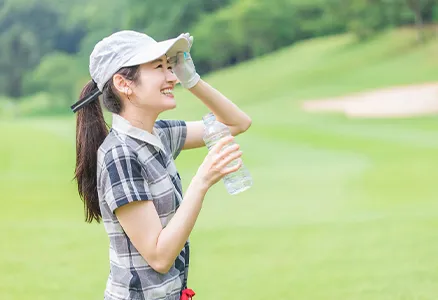 ゴルフ場でペットボトルの水を持ち微笑む女性の写真